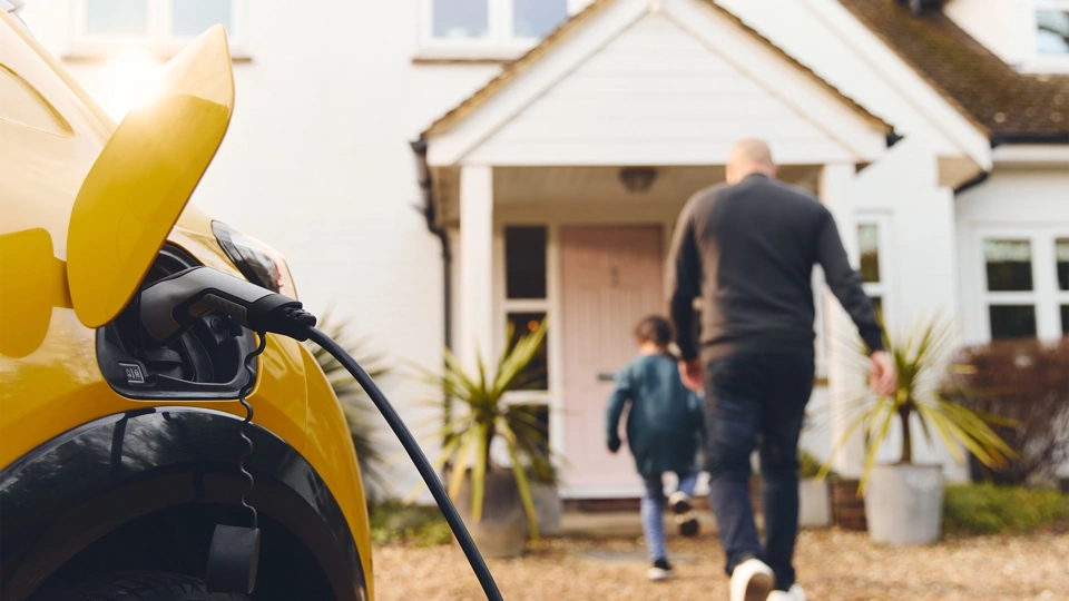 Yellow car being charged in driveway while a man and boy enter the house