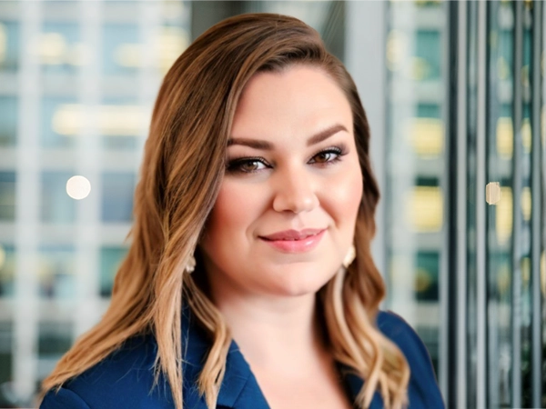Portrait of Kelly Wheeler, Senior Project and Programme Manager, with city landscape featuring building with lots of windows in the background.