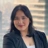 Portrait of Nanda Angelina, Marketing and Communications Coordinator, Asia, Smiling in office space against window, where blurry figures of other offices buildings are shown.