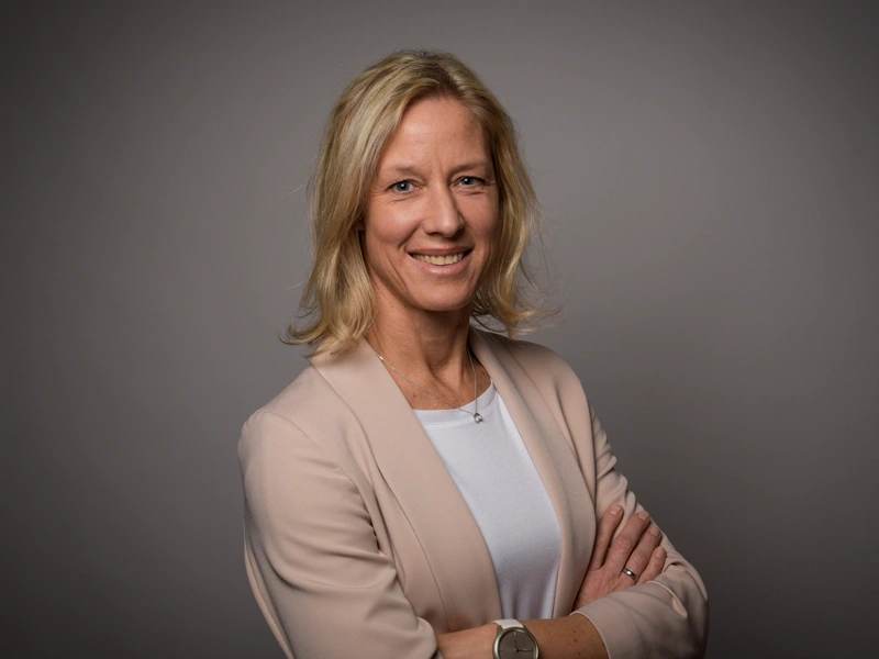Portrait of Bettina Würfel, managing director, Germany and Austria, smiling in white shirt against office background with sunshine shinning through window.