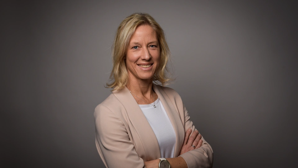 Portrait of Bettina Würfel, managing director, Germany and Austria, smiling in white shirt against office background with sunshine shinning through window.