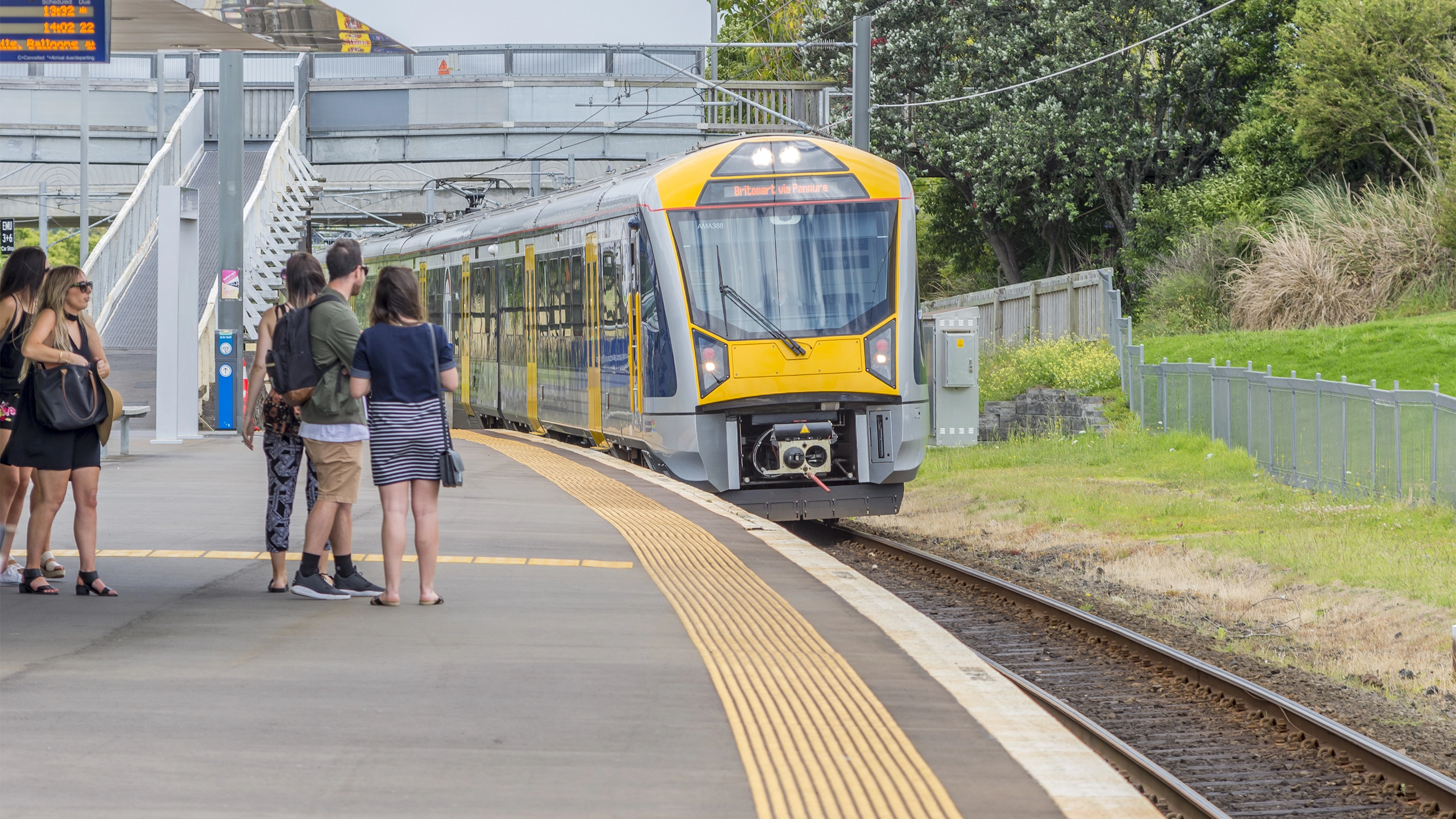 Yellow train entering a station with people waiting on the platform