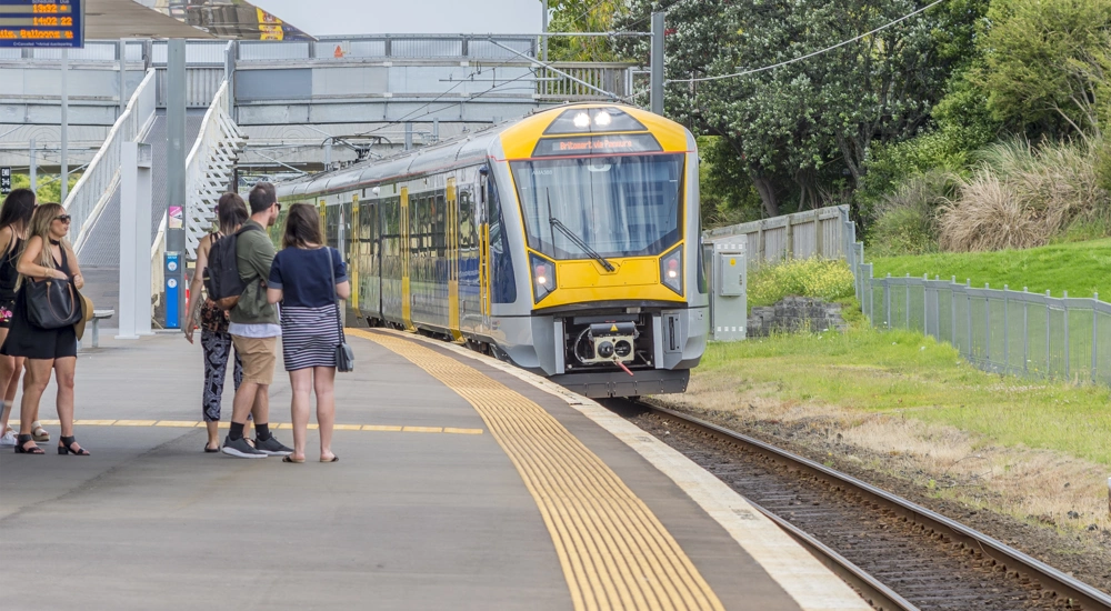 Yellow train entering a station with people waiting on the platform