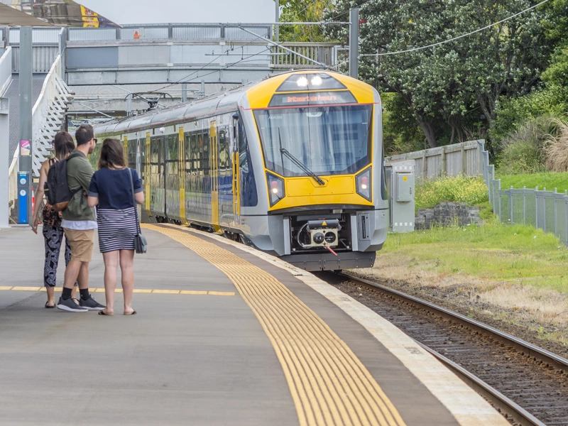 Yellow train entering a station with people waiting on the platform