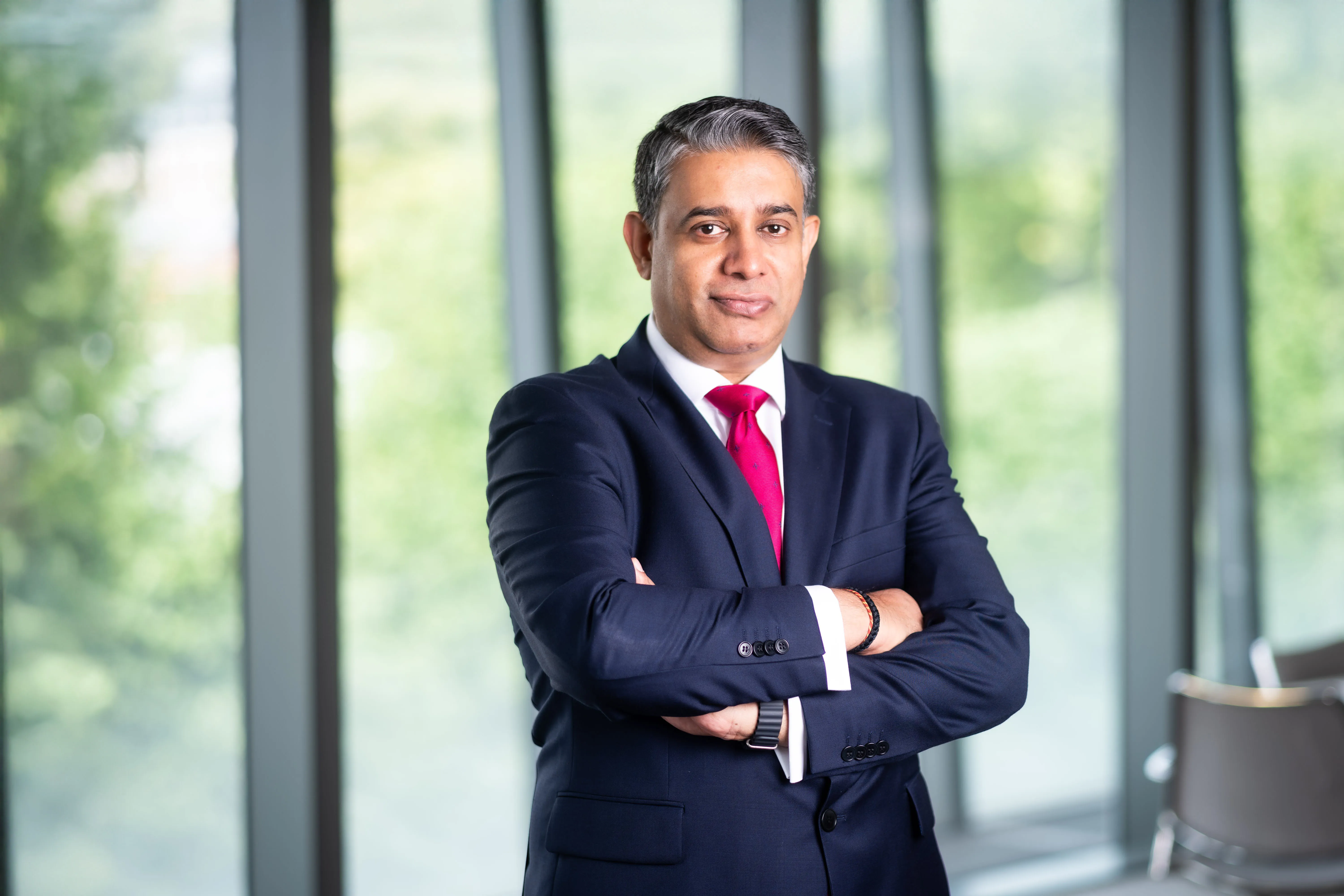 Anooj Oodit, Managing Director, Americas, in front of a window with a view of trees
