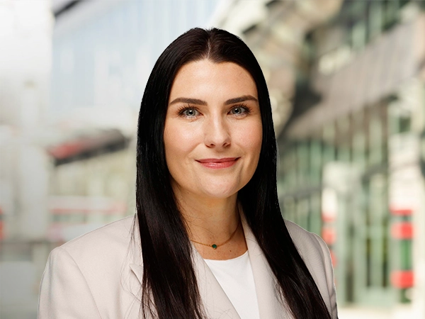 Portrait of Tiffany Emmett, Associate Director, Construction Economics, standing outside in front of buildings featuring an urban cityscape with a mix of architectural styles. The scene includes some windows and red features, adding a touch of color.