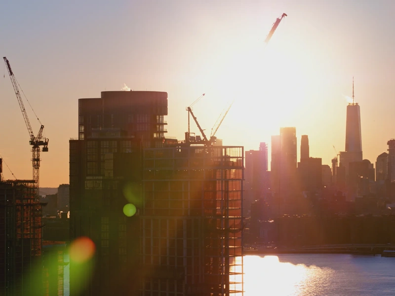 New residential towers' construction on the waterfront in Brooklyn, with the scenic view of Manhattan skyline, at sunset.