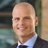 Brad Moolman, Associate Director, outside in front of a blurred brown background featuring a building and mix of natural and urban elements.