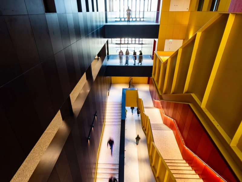 Yellow and red staircase in a black building with people chatting and walking down.