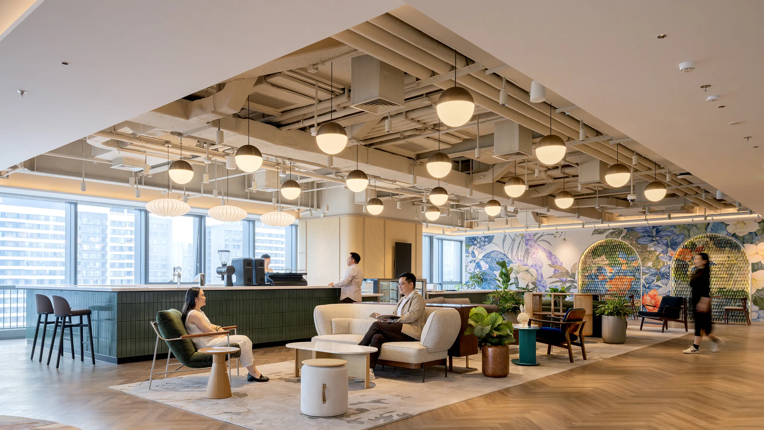 Modern office lounge with a coffee bar, seating area, warm lighting, wooden floors and colourful walls.