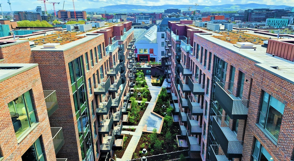 An aerial shot of a cluster of modern flats, with blue skies and small gardens.
