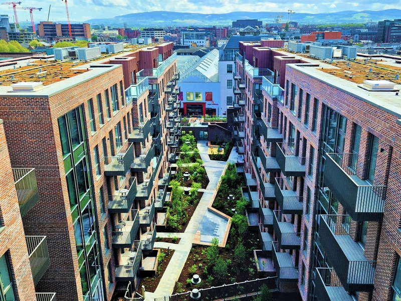An aerial shot of a cluster of modern flats, with blue skies and small gardens.