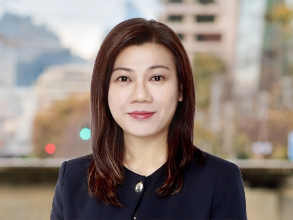 Cheryl Lum, Director, Cost Management, Singapore, outside in front of a blurred brown background featuring a building and mix of natural and urban elements.