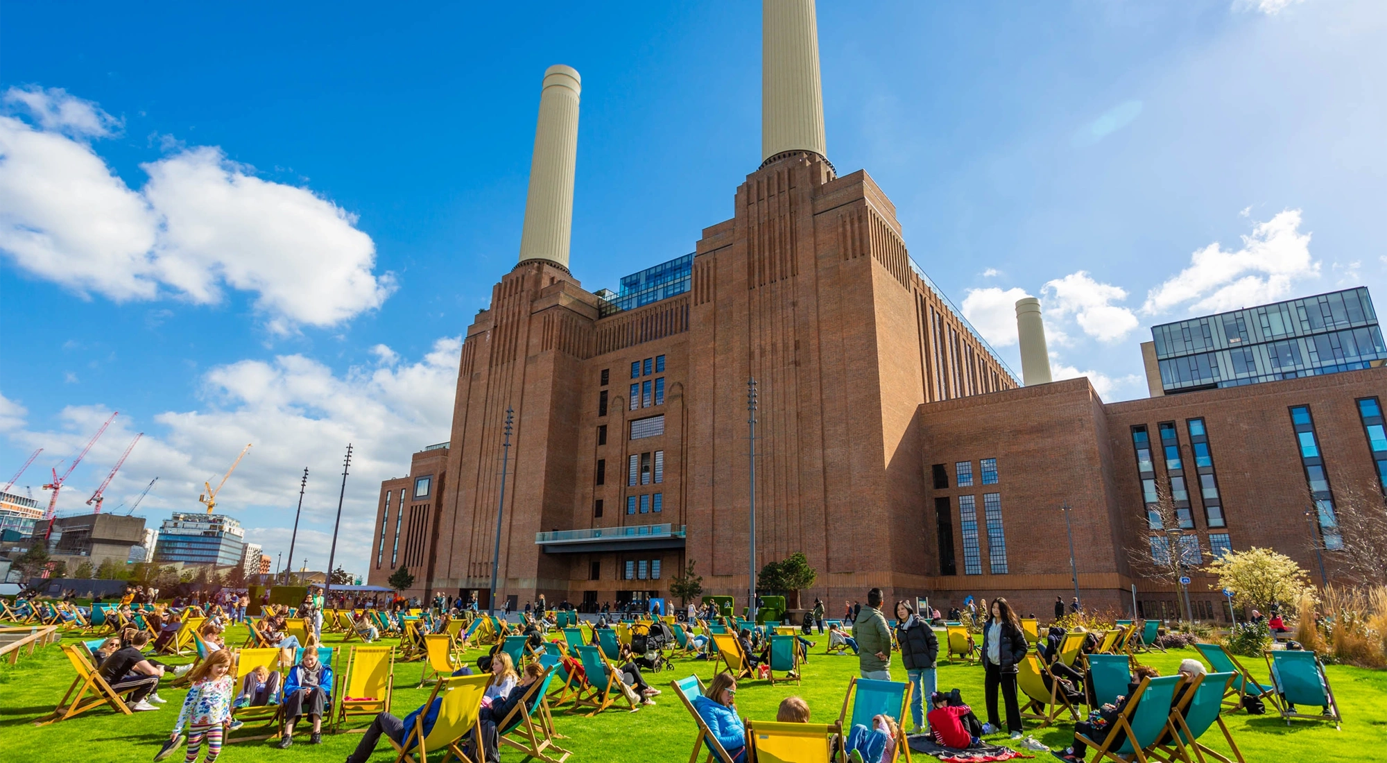 Group of people sitting outside in deck chairs in front of Battersea Power Station on a sunny day