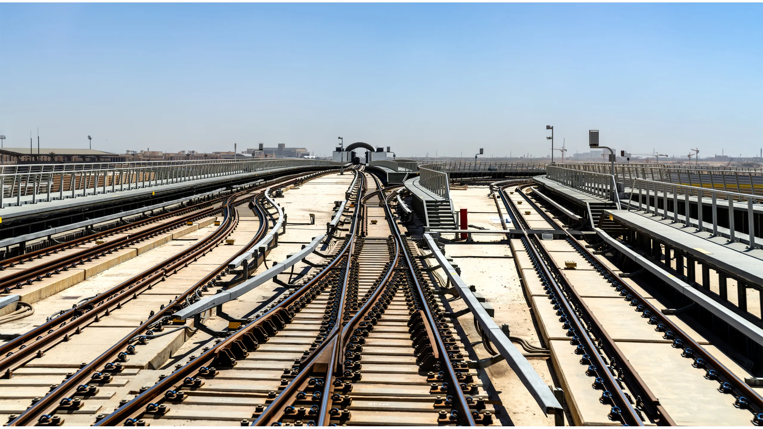 A view of the Riyadh Metro railway tracks and rail switches leading to a maintenance depot under a clear blue sky.