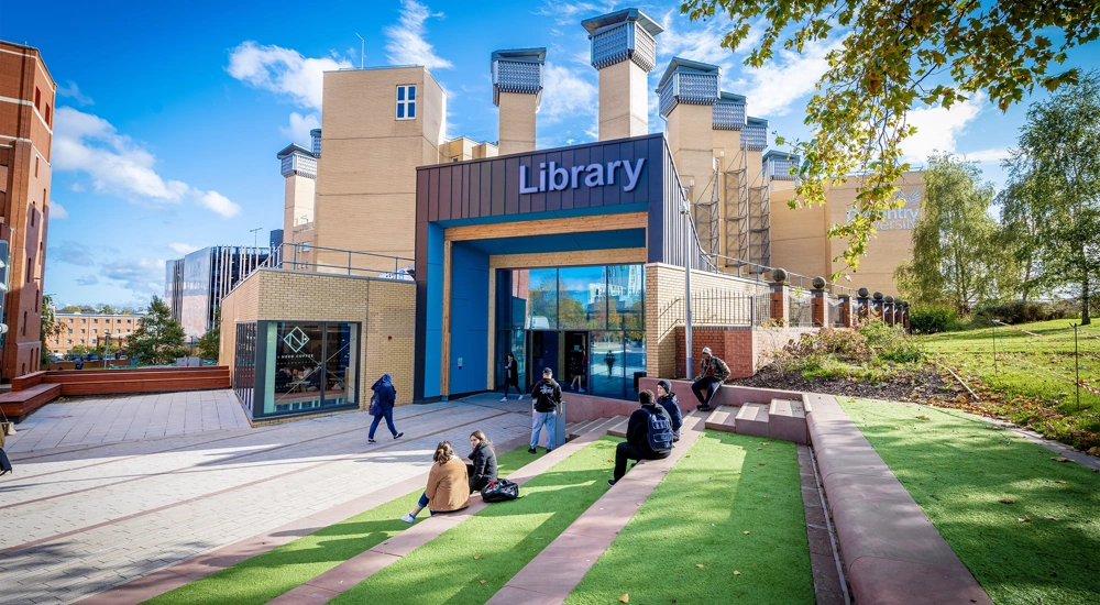 Students sitting on a lawn and stairs outside a library building