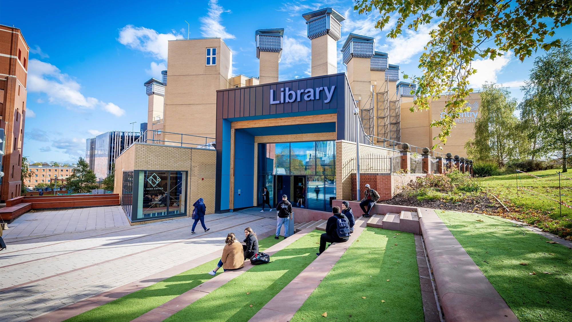 Students sitting on a lawn and stairs outside a library building