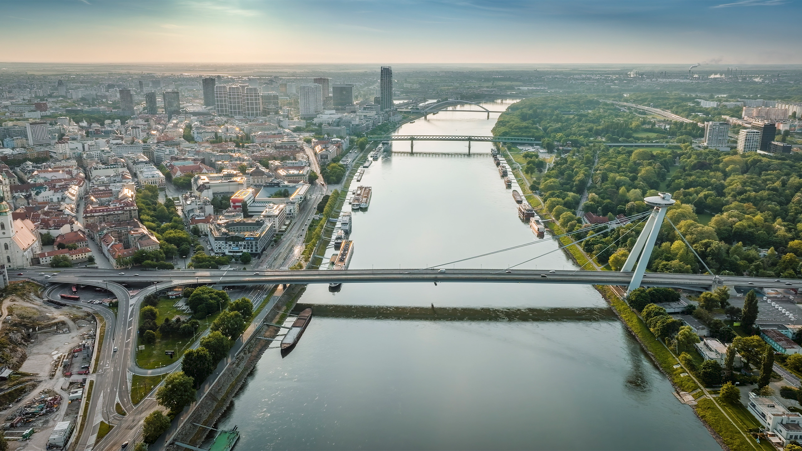 Aerial view of river with multiple bridges, surrounded by city buildings and green park area.