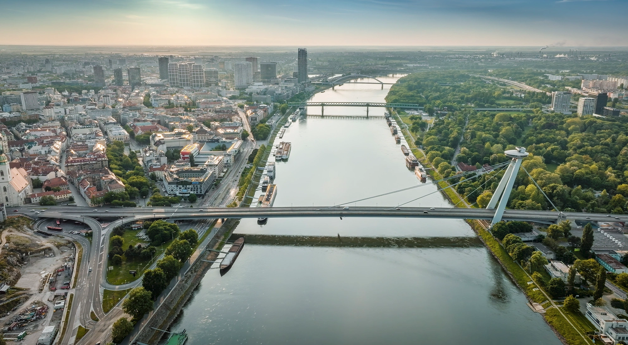 Aerial view of river with multiple bridges, surrounded by city buildings and green park area.