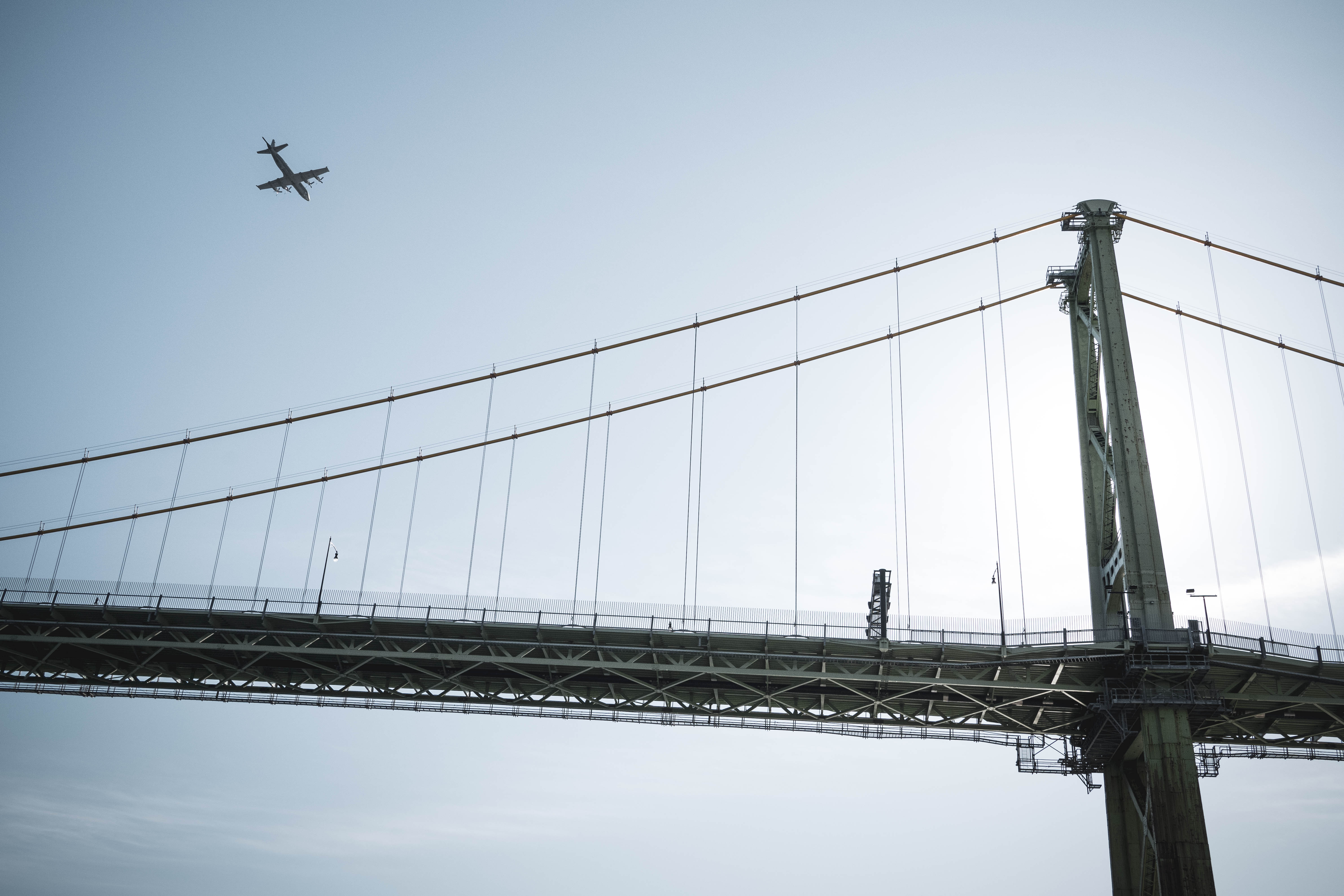 View of bridge against blue sky with plane in the background.