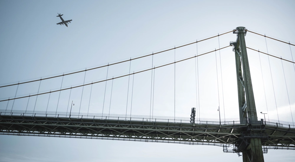 View of bridge against blue sky with plane in the background.