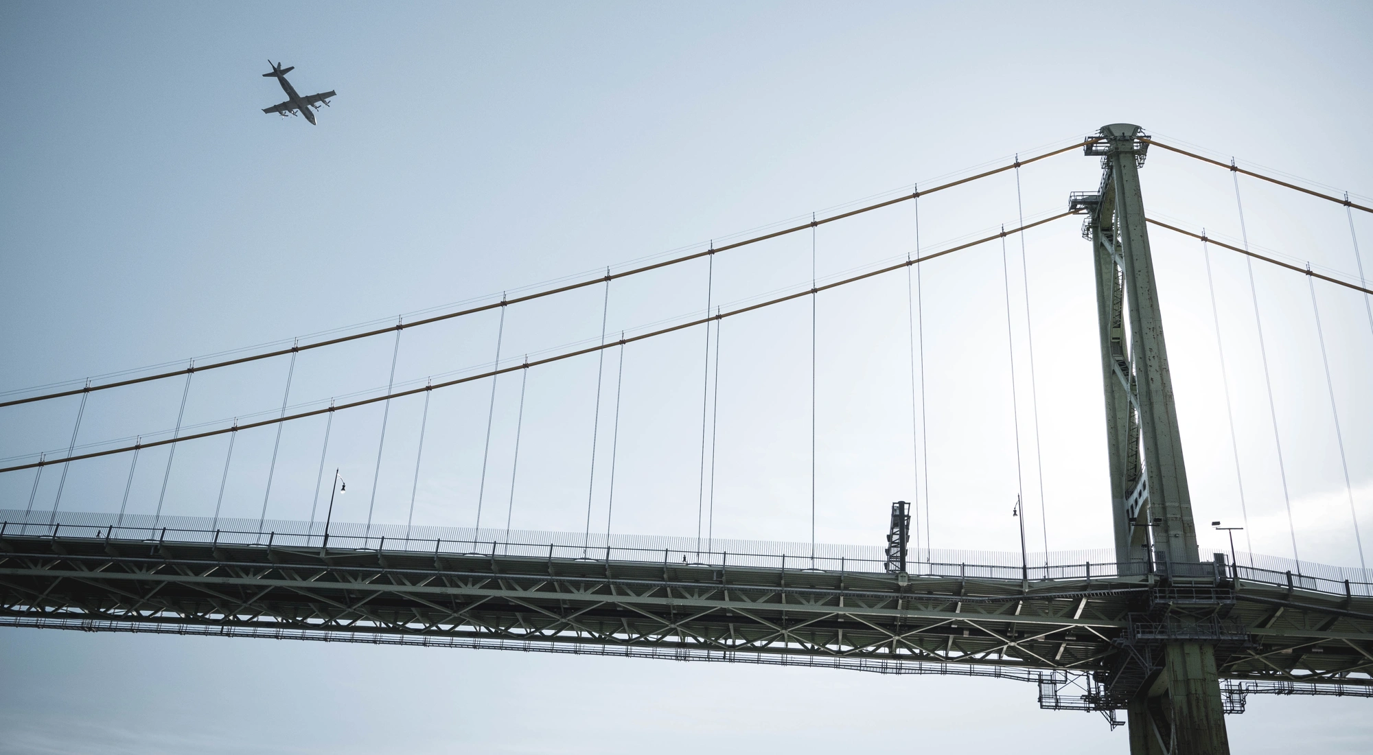 View of bridge against blue sky with plane in the background.