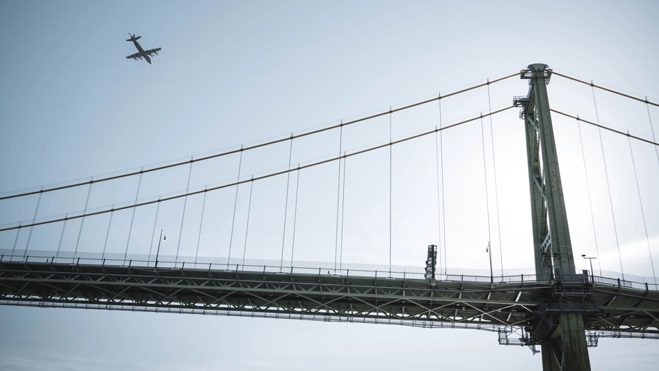 View of bridge against blue sky with plane in the background.