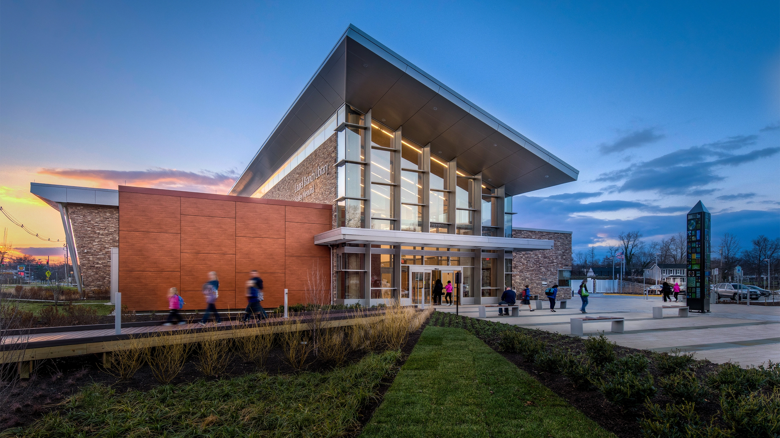 Exterior photo of a standalone library building with groups of people entering and exiting