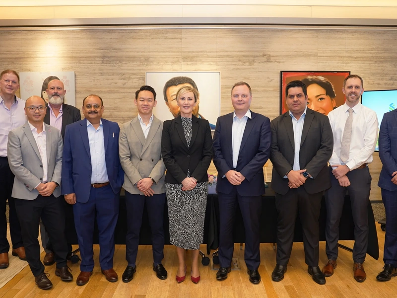 Group of ten colleagues standing for a photo, smiling. There are nine males and a female colleague in the middle. There are also pieces of artwork hanging in the back.