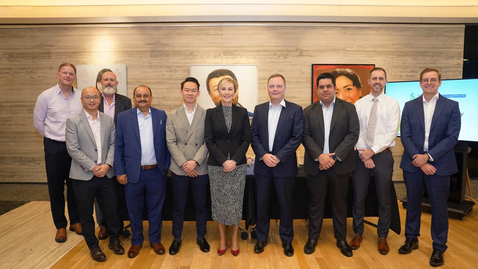 Group of ten colleagues standing for a photo, smiling. There are nine males and a female colleague in the middle. There are also pieces of artwork hanging in the back.