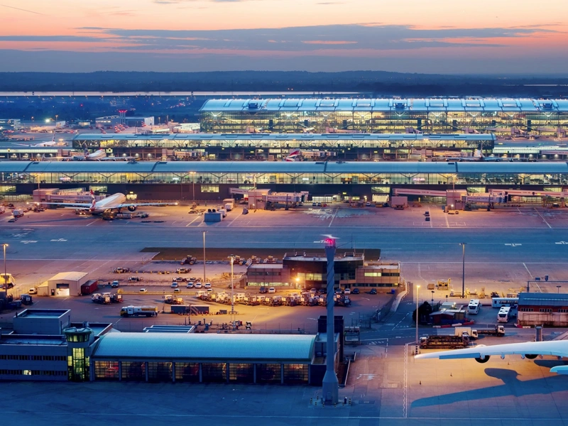 Heathrow airport featuring an airplane, bright lights in the building and orange sunset in the background