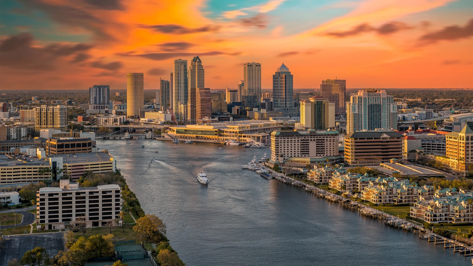 Ariel view of city skyline at sunset with boats on river.