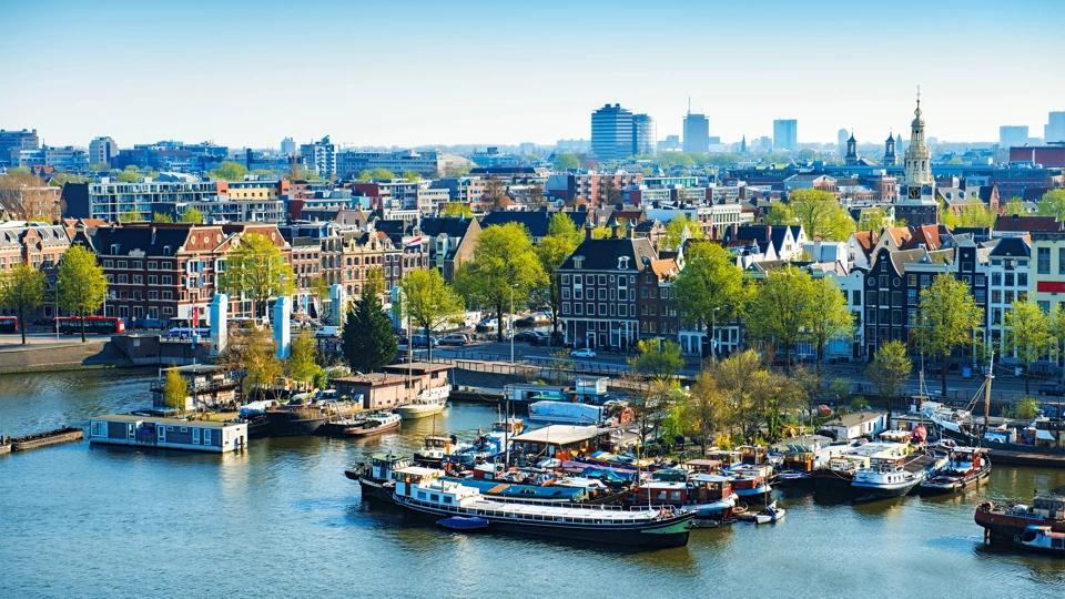 Aerial View of Amsterdam city on One Beautiful Sunny Day. View of Amsterdam rooftops, also visible are many bridges, harbor, boats, yachts, canals, restaurants, bikes, churches and typical dutch houses in Centrum. Amsterdam, Netherlands.