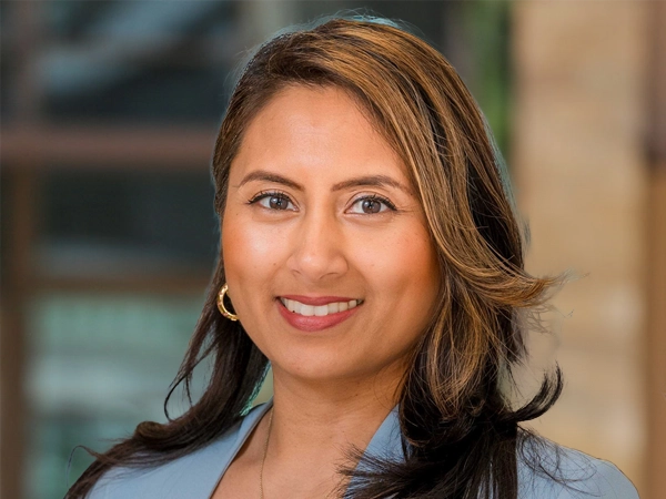 Portrait of Mireille Thakoersingh, Marketing and Communications Manager, outside in front of a blurred brown background featuring a building and mix of natural and urban elements.