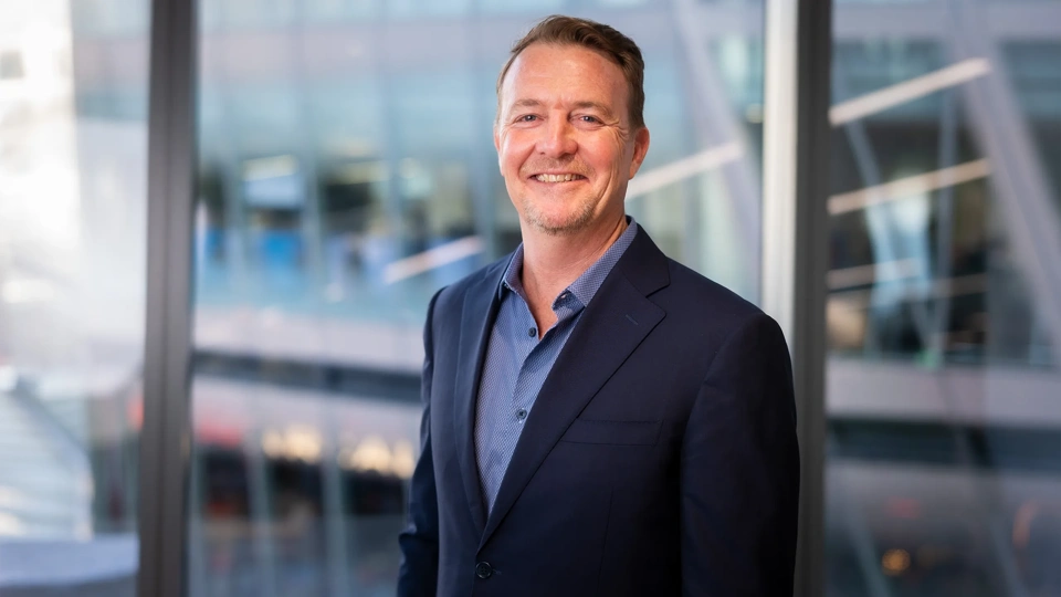 Portrait of Tim White, Regional Managing Director, Africa, standing in from of windows in office in blue suit, smiling.