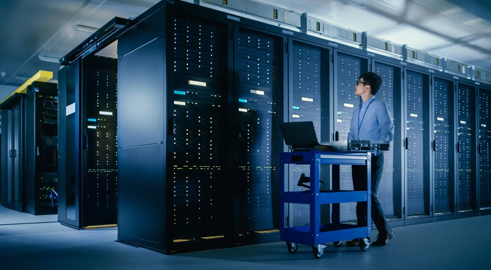 In the Modern Data Center: IT Engineer Doing Maintenance and Diagnostics. Pushes Cart alongside Server Racks, Ready to Install New Hardware for Planned System Update, Equipment Replacement.