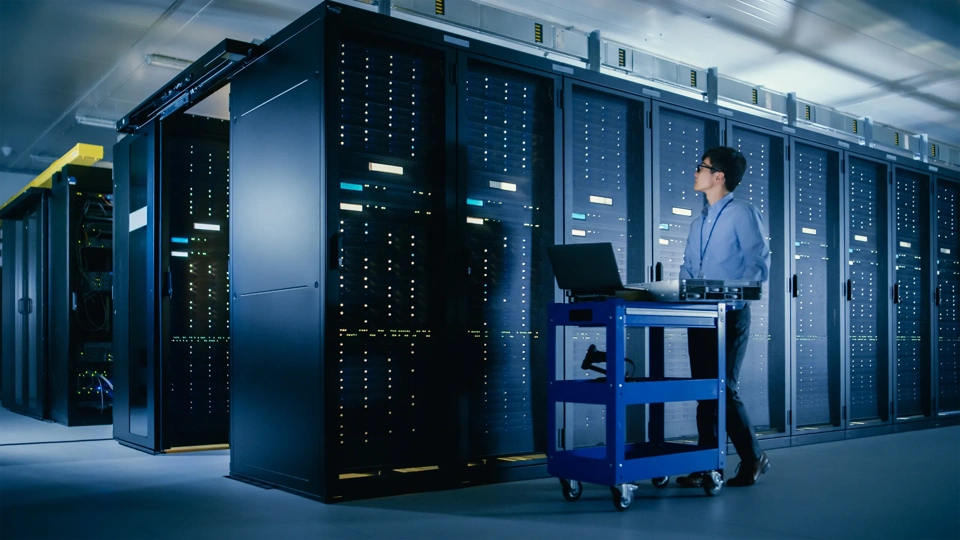 In the Modern Data Center: IT Engineer Doing Maintenance and Diagnostics. Pushes Cart alongside Server Racks, Ready to Install New Hardware for Planned System Update, Equipment Replacement.