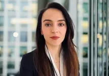 Portrait of Gabriela Mariniuc, Associate Director, standing in window based office building smiling.