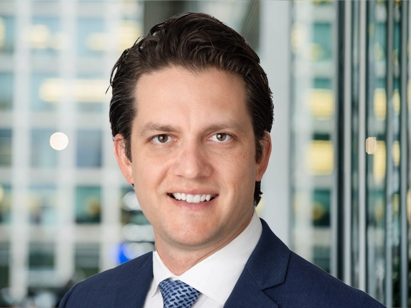 Portrait of Drew Ference, Director, Real Estate, North America, with city landscape featuring building with lots of windows in the background.