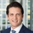 Portrait of Drew Ference, Director, Real Estate, North America, with city landscape featuring building with lots of windows in the background.