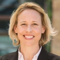 Lisa Woodruff, Executive Vice President, Global Head of Retail, outside in front of a blurred brown background featuring a building and mix of natural and urban elements.
