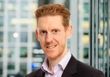 Portrait of Gary Healey, Director, with city landscape featuring building with lots of windows in the background.