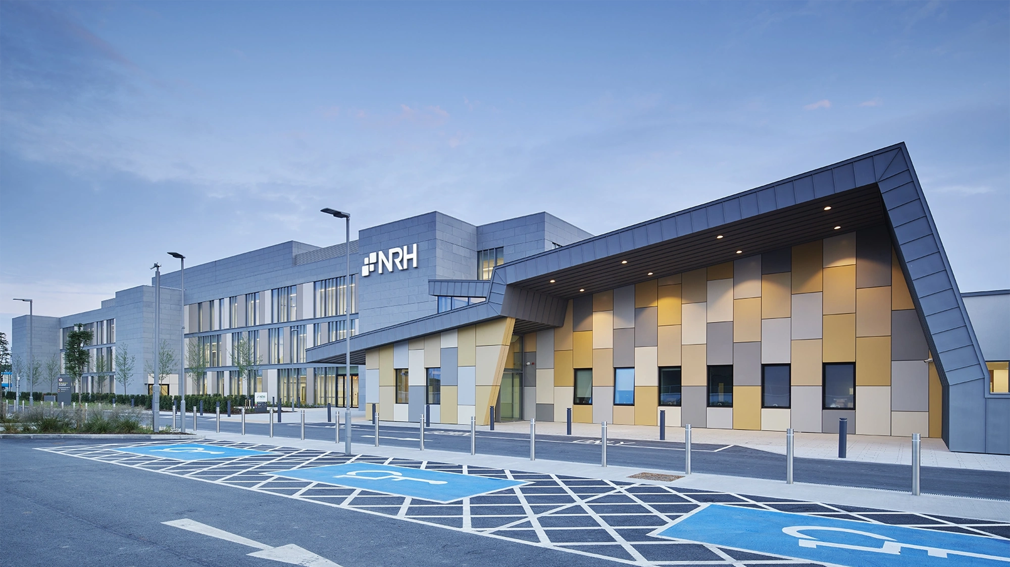 Big building with colourful yellow and grey square tiles with brand name NRH on it, and disabled parking outside
