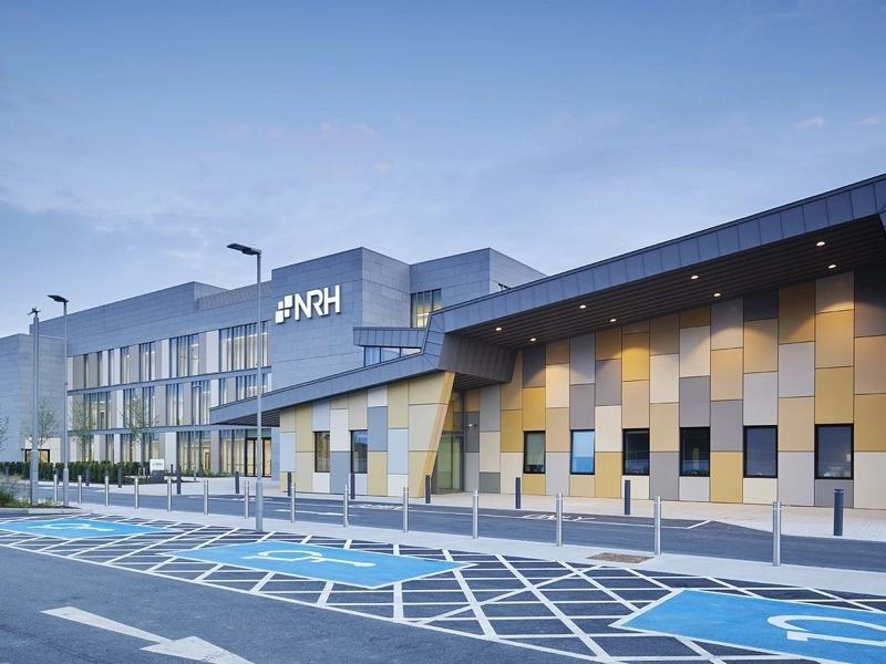 Big building with colourful yellow and grey square tiles with brand name NRH on it, and disabled parking outside