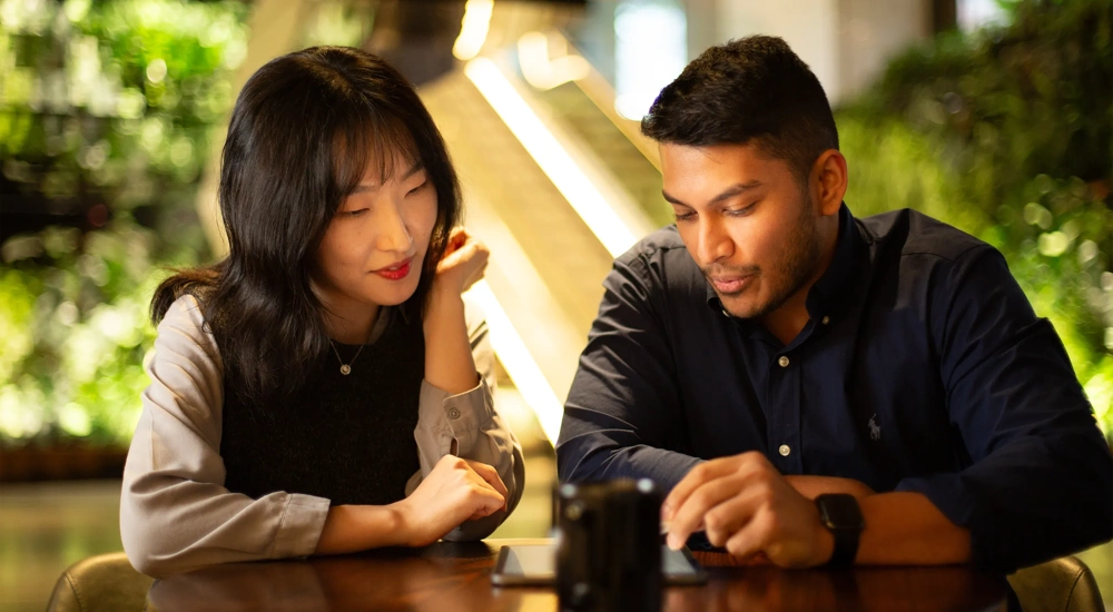 Two colleagues together looking at a tablet in a plant-filled office.