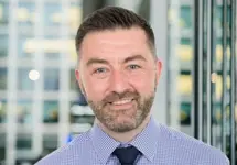 Portrait of Ewan Carmichael, Director, Technical Lead Performance Forum, Edinburgh, standing in window based office building.