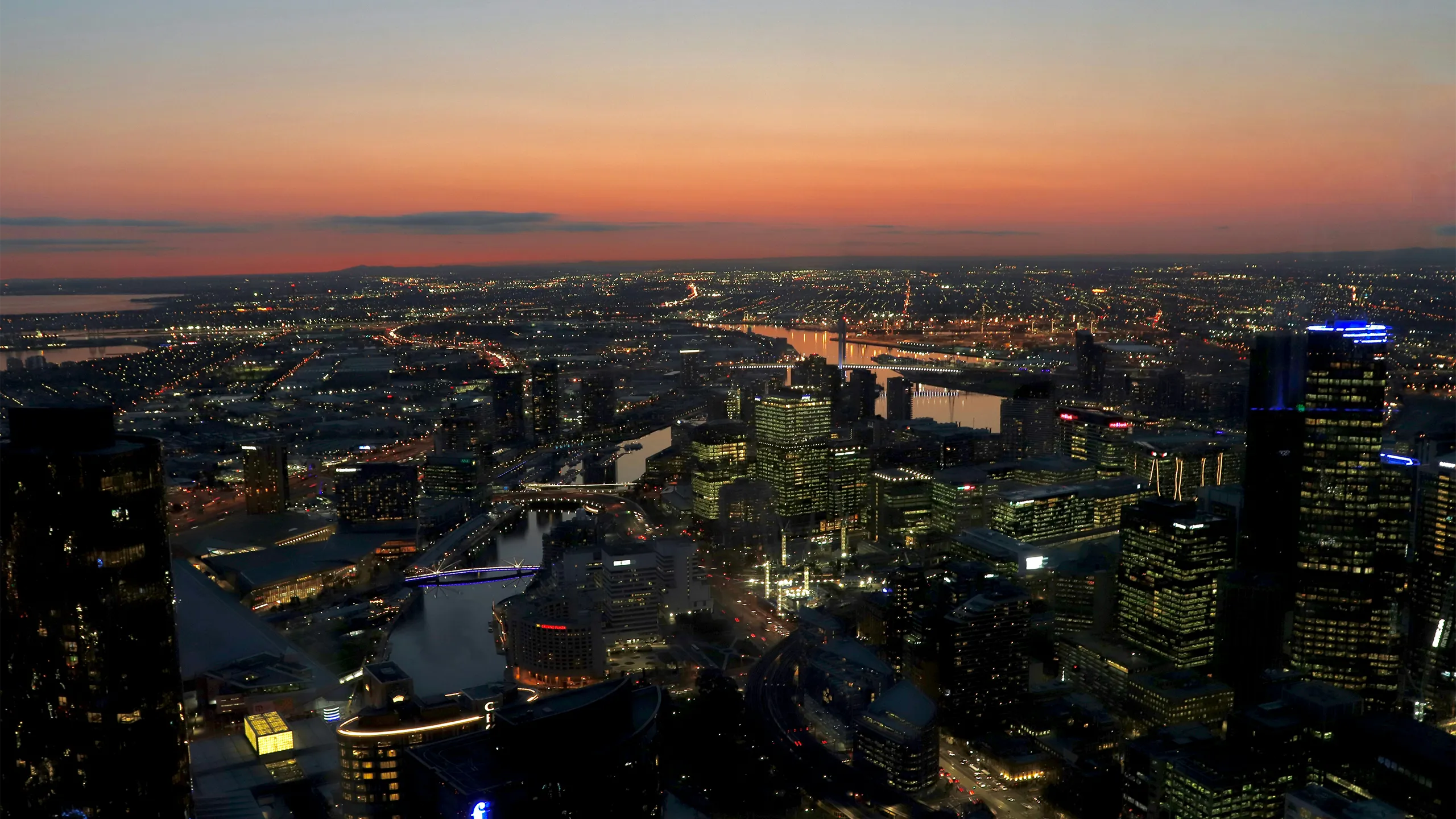 A breathtaking aerial view of Sydney's skyline at sunset, showcasing towering skyscrapers, a glowing sky, and serene waters in the distance