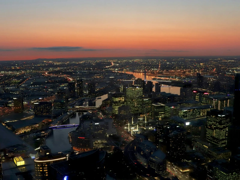 A breathtaking aerial view of Sydney's skyline at sunset, showcasing towering skyscrapers, a glowing sky, and serene waters in the distance