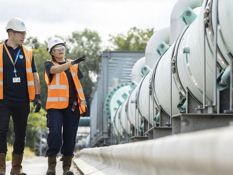 Smiling contractors walking along rows of concrete mixer trucks and planning working day at construction site