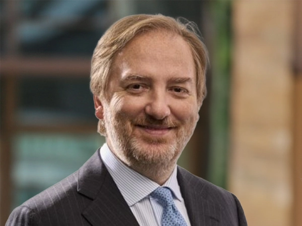 Carlo Matildi, Managing Director, outside in front of a blurred brown background featuring a building and mix of natural and urban elements.